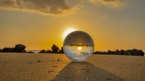 Close-up of crystal ball on beach against sky during sunset