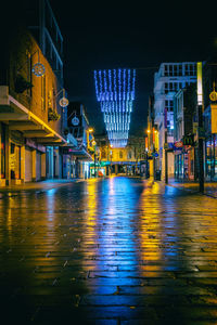 Illuminated road by buildings in city at night