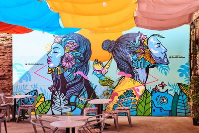 Multi colored chairs on table against graffiti wall