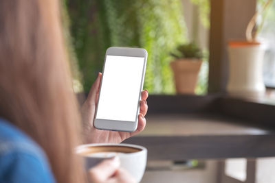 Cropped image of woman holding coffee cup and mobile phone at home