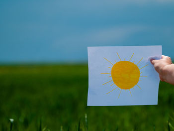 Person holding yellow leaf on field against sky