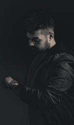 Young man looking away while standing against black background