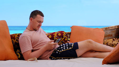 Midsection of man sitting on sea against sky