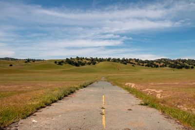 Dirt road amidst field against sky