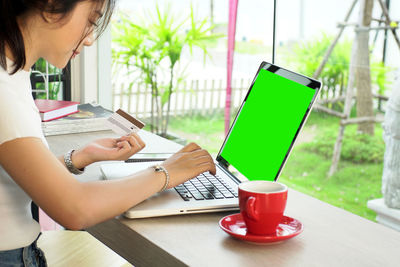 Young woman holding credit card while using laptop at home