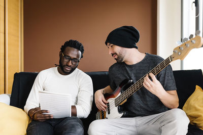 Friends looking at sheet music while sitting on sofa