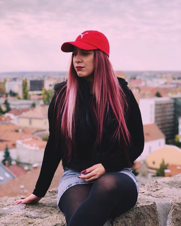 PORTRAIT OF BEAUTIFUL WOMAN SITTING AGAINST BUILDINGS