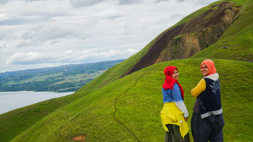 Rear view of two women on green landscape against sky