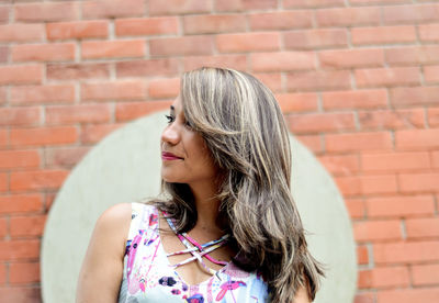 Young woman looking away while standing against wall