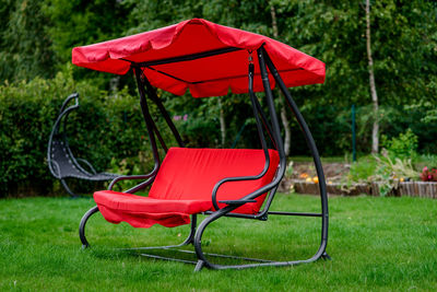 Empty red swing bench on grassy field at yard