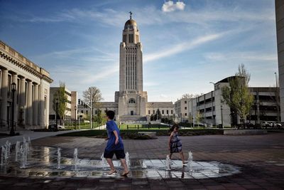 Cheerful boy and girl standing at fountain in city against sky