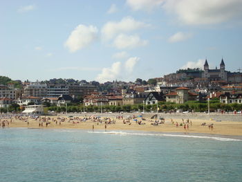 People on beach by city against sky