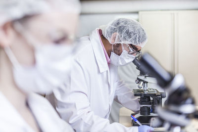 Man and woman scientists looking through microscope at laboratory