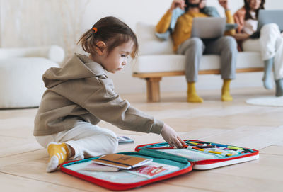 Cute little girl draws against background of working parents on laptops at home