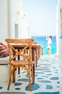 Empty chairs and table at beach against sky