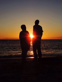 Silhouette men standing at beach during sunset
