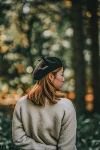 Woman looking away while standing against trees