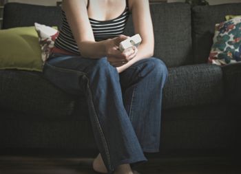 Midsection of woman holding remote control while sitting on sofa at home
