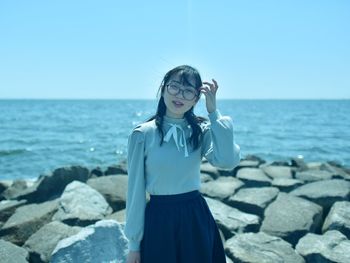 Young woman standing on rock at beach against sky