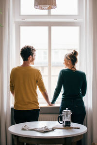 Rear view of romantic couple standing at window in living room