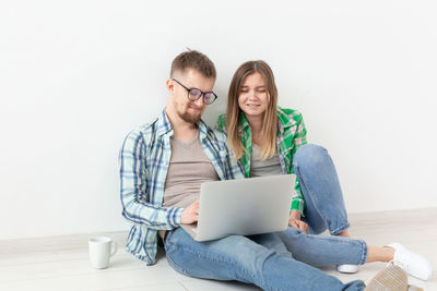 Young woman using phone while sitting on laptop