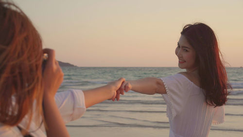 Lesbian couple holding hands on beach against sky