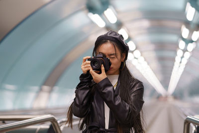 Young stylish korean girl make photos on camera in urban transport riding escalator while travelling