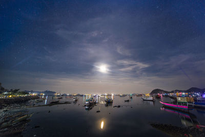 Illuminated city by sea against sky at night