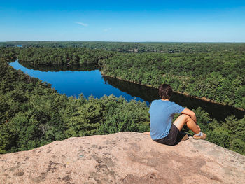 Teen boy sitting on the rocky summit of a hiking trail on a sunny day.