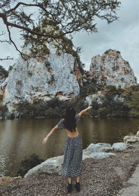 Rear view of woman standing on rock by lake against sky