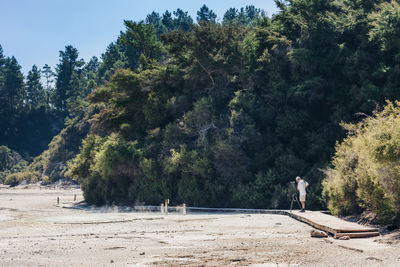 Full length of man photographing while standing on boardwalk against trees