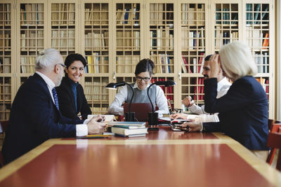 Happy male and female lawyers sitting in board room against bookshelf