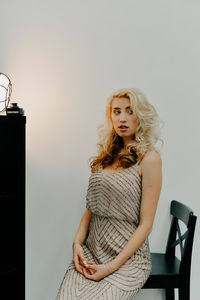 Portrait of a young woman sitting against wall