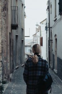 Rear view of woman walking on street amidst buildings in city