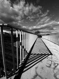 Shadow of railing on bridge against sky