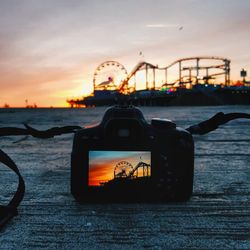 Close-up of camera on beach against sky during sunset