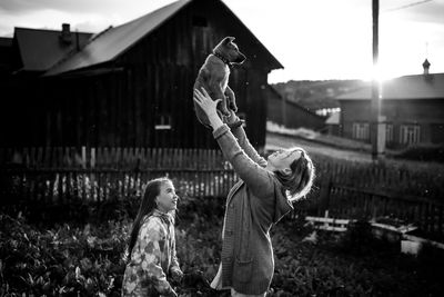 Rear view of people with arms raised and flying dog, black and white photography