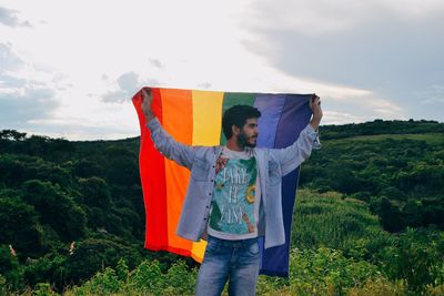 Man holding rainbow flag against sky