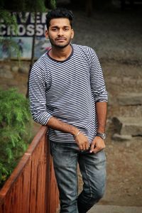 Portrait of young man standing by railing