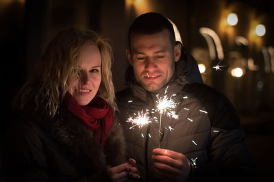 Close-up of young couple holding sparklers at night
