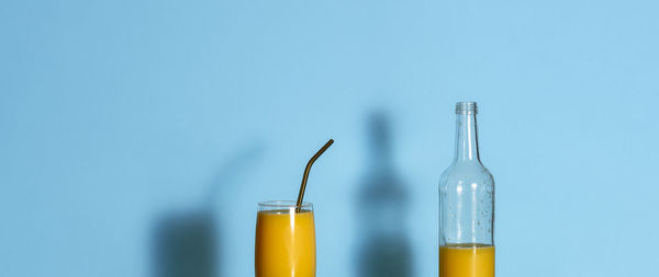 Glass of orange juice and empty bottle on blue background. orange juice in a glass and metal straw. 