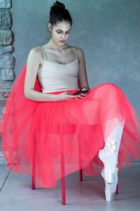 Full length of ballet dancer sitting on chair while using phone