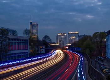 Light trails on road amidst buildings against sky at night