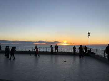 Silhouette people on sea against sky during sunset