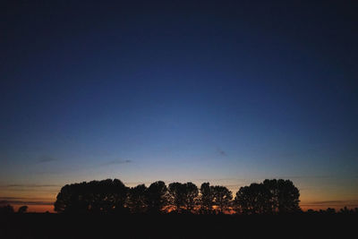 Silhouette trees on field against clear blue sky