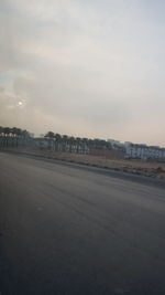 Road by buildings against sky during sunset