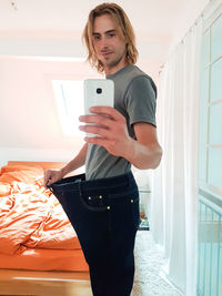 Young woman using phone while standing on bed at home
