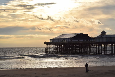 Silhouette person standing at beach against cloudy sky during sunset