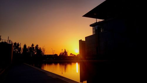 Silhouette buildings by lake against sky during sunset