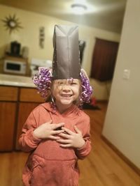 Portrait of smiling girl wearing paper bag while standing at home